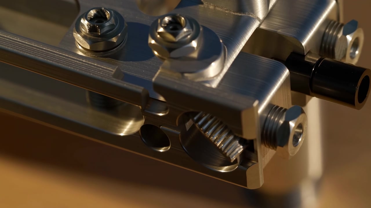 Close-up composition moves laterally over brushed metal hardware, keeping reflective bolts, small gear teeth, and dark cylindrical fitting against a softly blurred amber background.