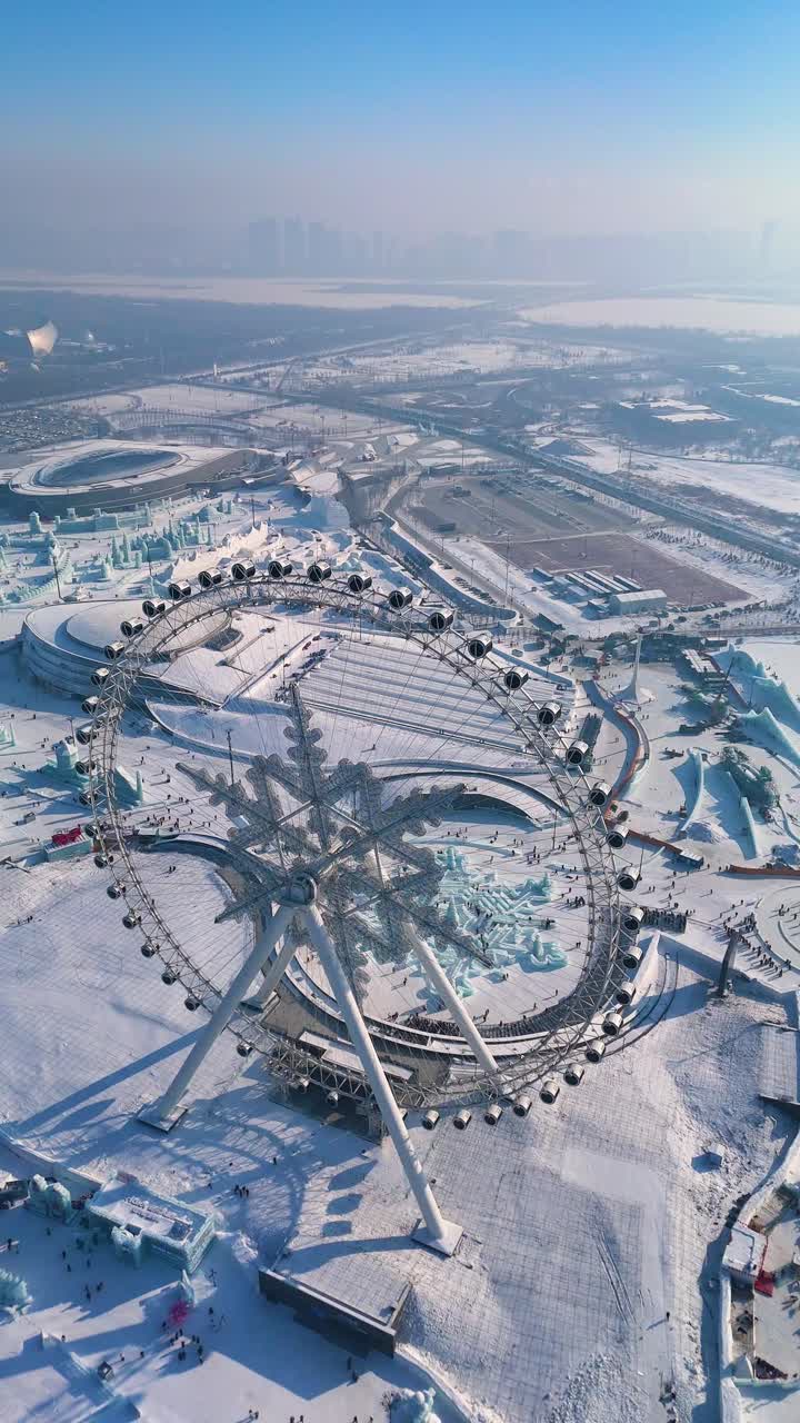 Vertical slow pull-in drone shot of the Snowflake Ferris Wheel at the Harbin Ice Festival 2025. Snowy cityscape in the background. China