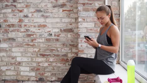 woman relaxing at a window seat in a gym, using phone
