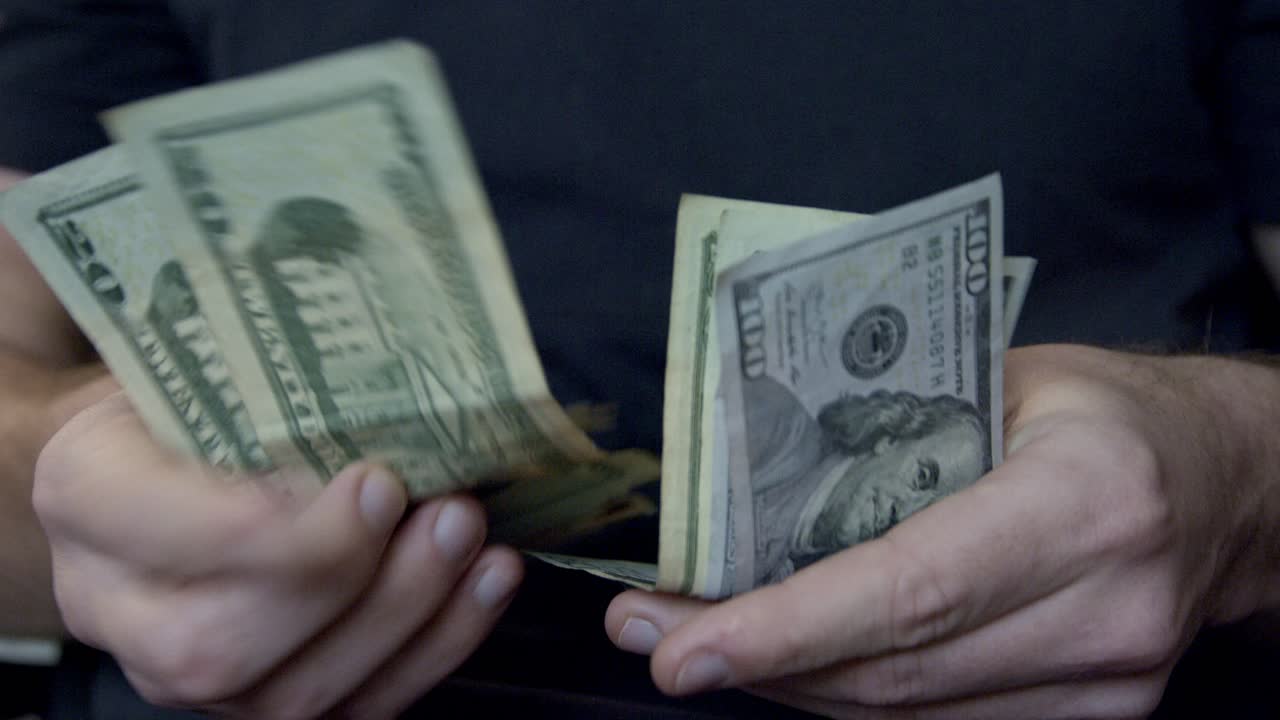 Nærbillede af hånd, der tæller pengesedler – udfoldede amerikanske dollars, der tælles.