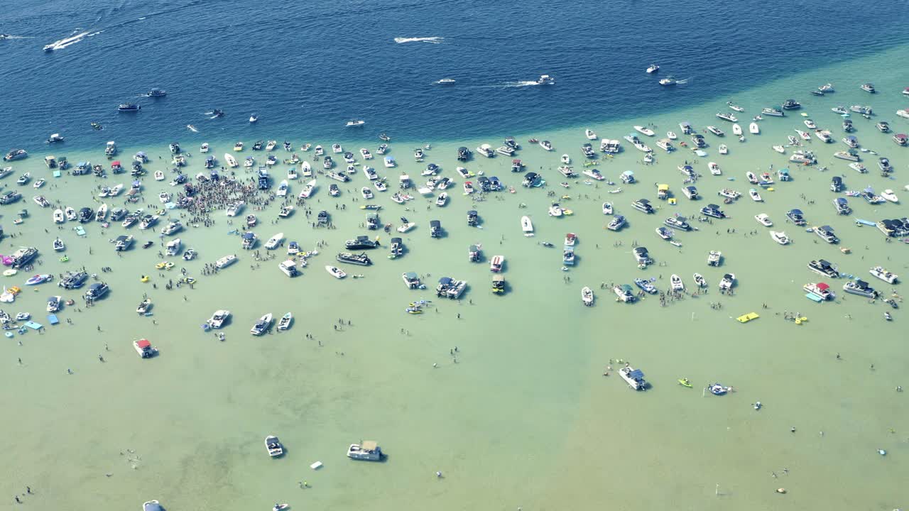 Aerial shot of Boats and Large Group of People in shallow crystal clear Glacial Lake water on Sunny Summer Day Higgins Lake Michigan 4th of July