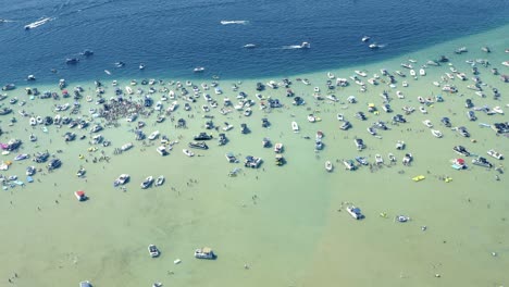 Toma-Aérea-De-Botes-Y-Un-Gran-Grupo-De-Personas-En-Agua-De-Lago-Glacial-Cristalina-Y-Poco-Profunda-En-El-Soleado-Día-De-Verano-Higgins-Lago-Michigan-4-De-Julio