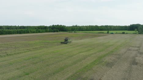 Aerial-establishing-view-of-combine-harvester-mowing-yellow-wheat,-dust-clouds-rise-behind-the-machine,-food-industry,-yellow-reap-grain-crops,-sunny-summer-day,-revealing-drone-shot-moving-backward