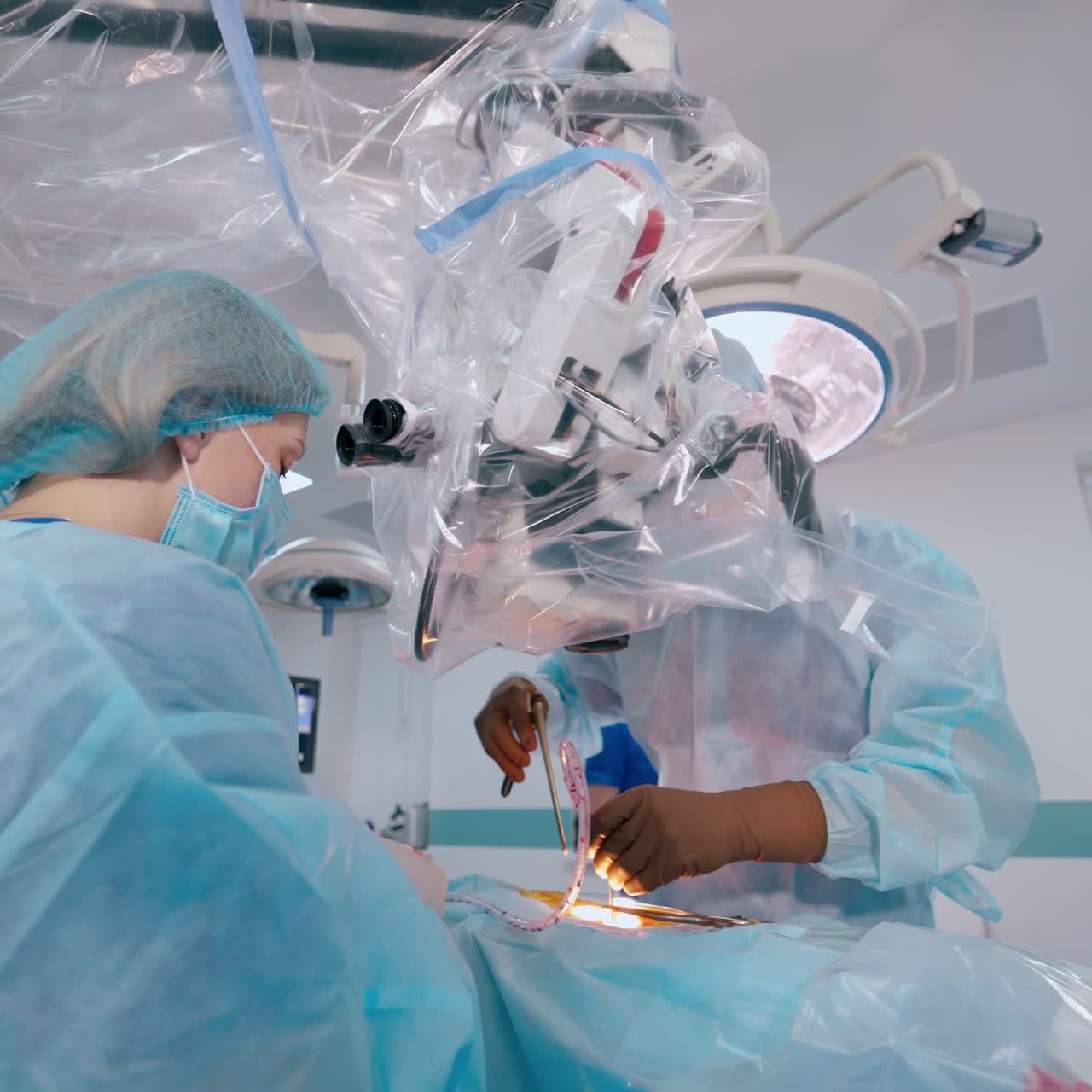 Surgical procedure. Professional doctor performing an operation while looking into the microscope. Nurse in medical uniform assists the surgeon.