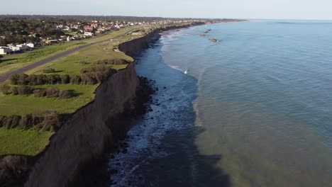 aerial flyover steep cliff face with driving cars on road and atlantic ocean in argentina during sunny day