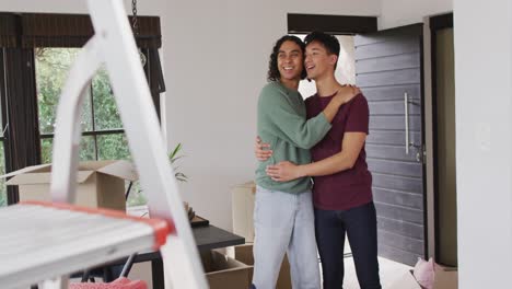 Happy-diverse-male-couple-moving-house,-talking,-embracing-and-smiling