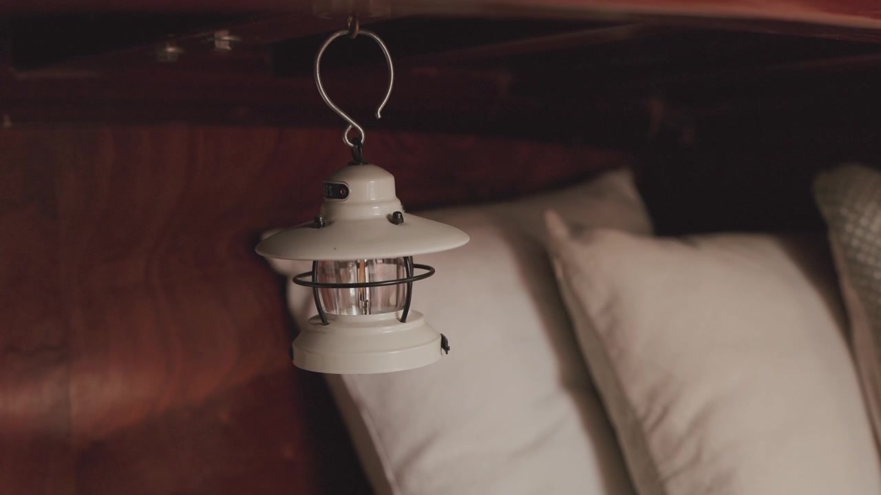 Linterna náutica blanca suspendida de un techo de madera oscura sobre almohadas blancas suaves.