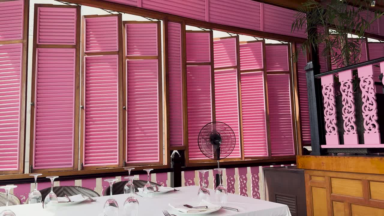 A serene dining setup with pink shutters and elegant tableware in a cliffside restaurant, capturing the essence of fine dining in Phuket