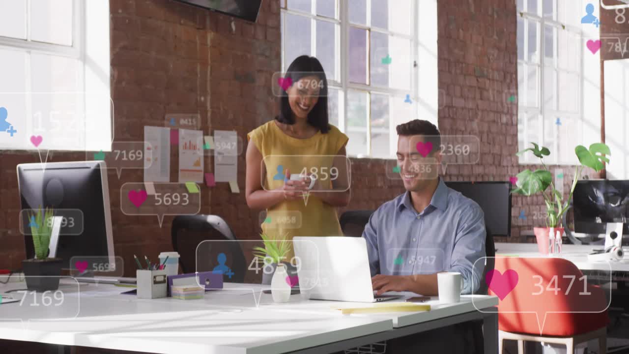 Floating social media icons around man typing while coworker shows smartphone boosting engagement