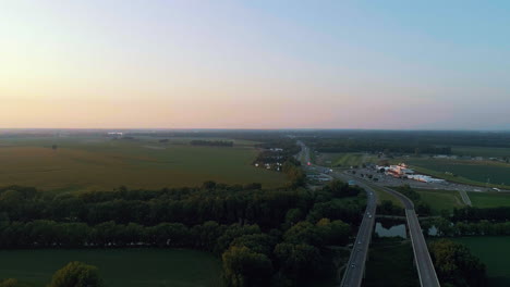 Toma-Aérea-De-La-Autopista-Estadounidense-Con-Campos-Rodantes-De-Indiana-En-El-Fondo