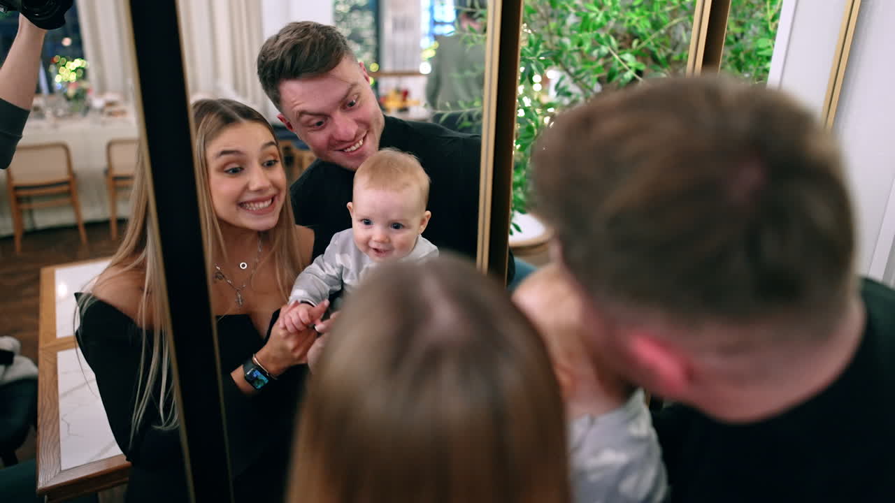 Loving parents holding a cute baby stand in front of the mirror. Family of three having fun together.