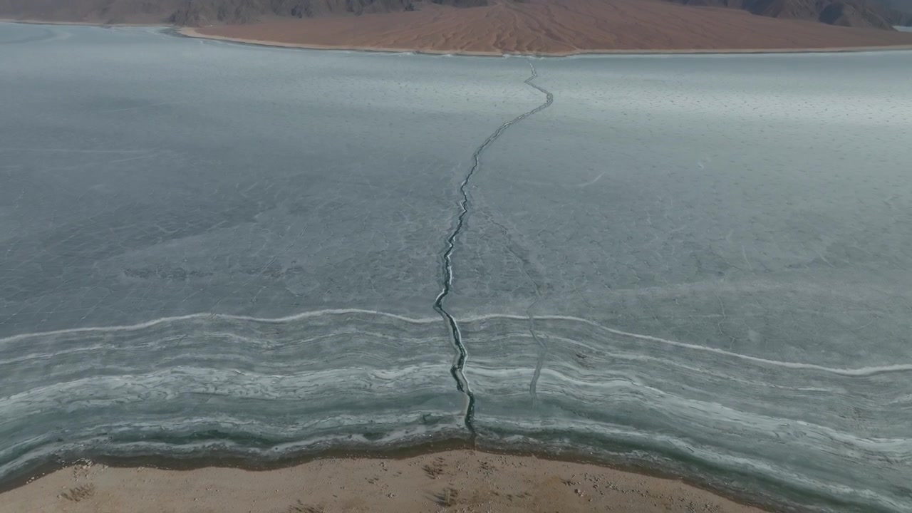 Aerial footage of the frozen Orto-Tokoy Reservoir with a long crack across the ice, surrounded by barren mountains in Issyk-Kul Region, Kyrgyzstan
