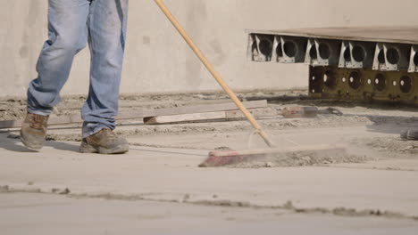 slow motion of construction worker in jeans and boots sweeping site debris