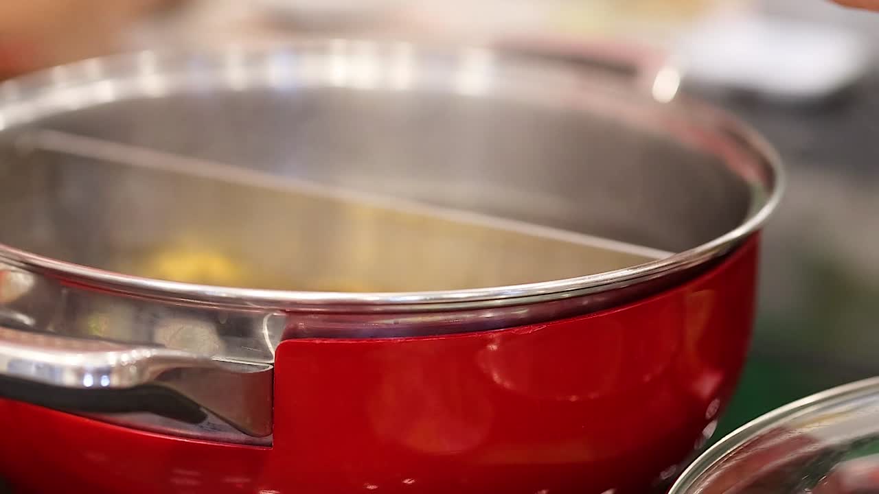 A hand stirs steaming soup in a shiny red pot, showcasing culinary preparation.