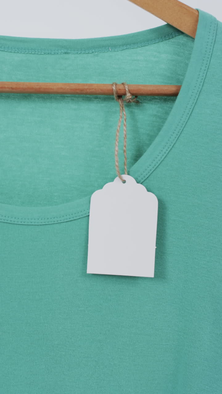 Vertical video of green t shirt with tag on hanger and copy space on white background