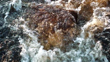 Mesmerizing-stream-of-water-hitting-rusty-stone-in-slow-motion,-top-down-view