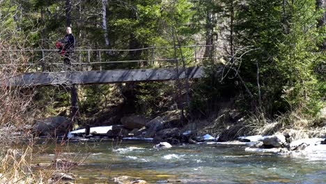 woman hiking across a bridge over a mountain stream