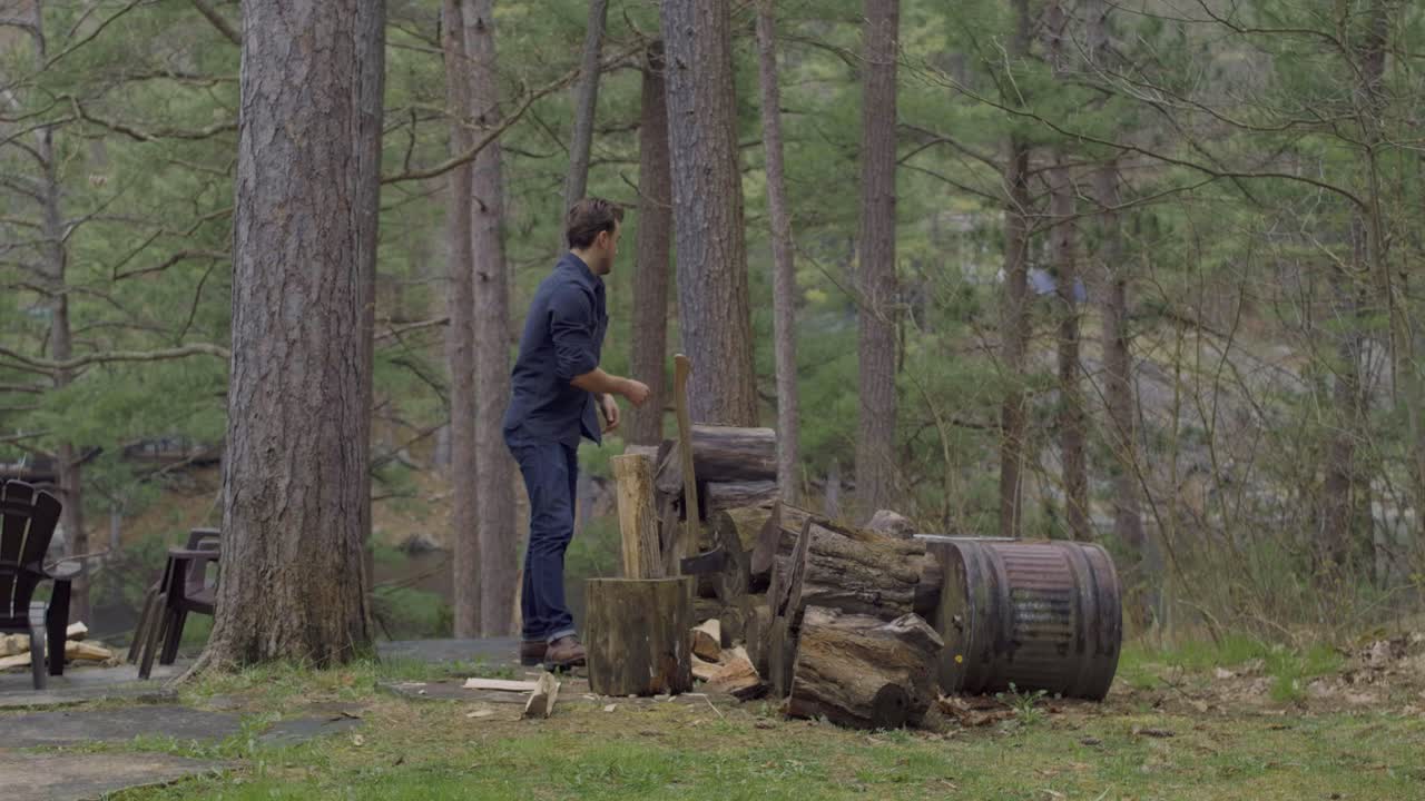 hombre cortando madera con un hacha en una claridad forestal, rodeado de árboles y una pila de troncos