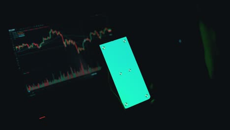 a trader holds a smartphone with a green screen in hands in a dark room. 4k