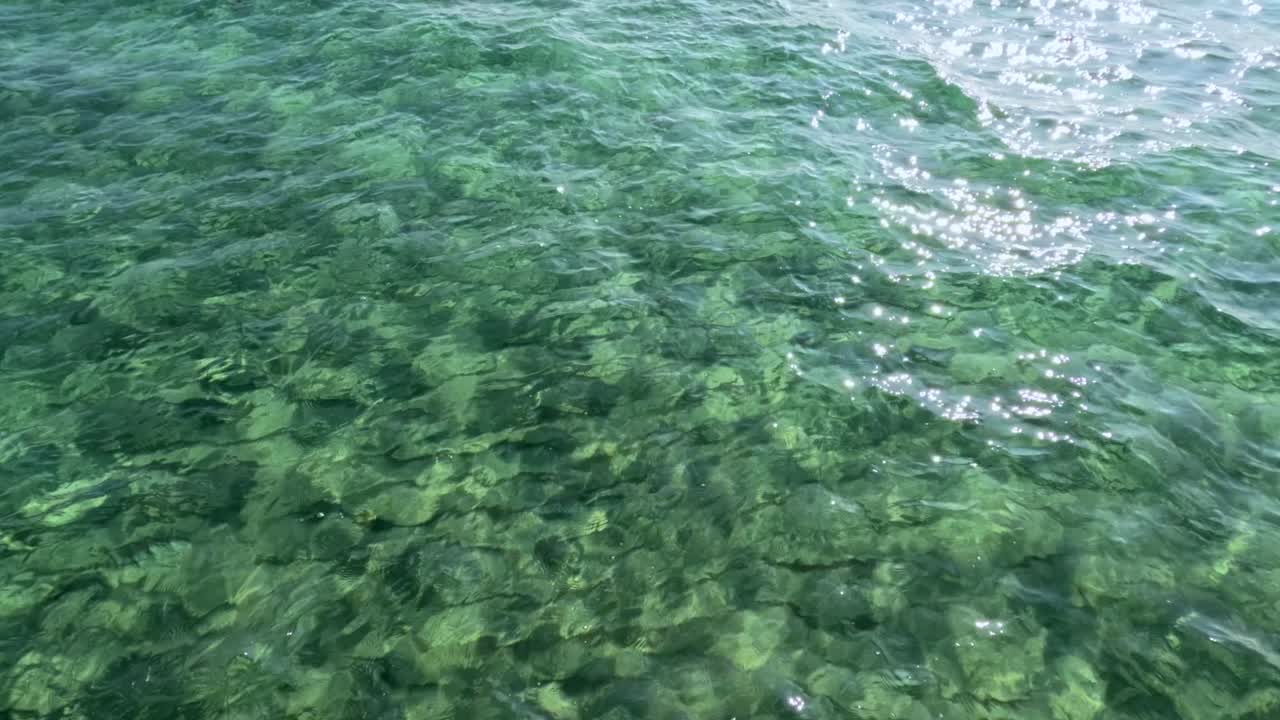 Aerial view of shimmering clear sea water with sunlight reflections, showcasing natural beauty and tranquility