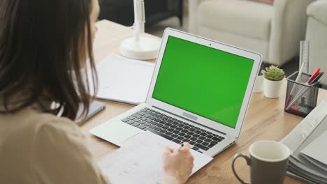 woman  video chatting on laptop with green screen and writing notes