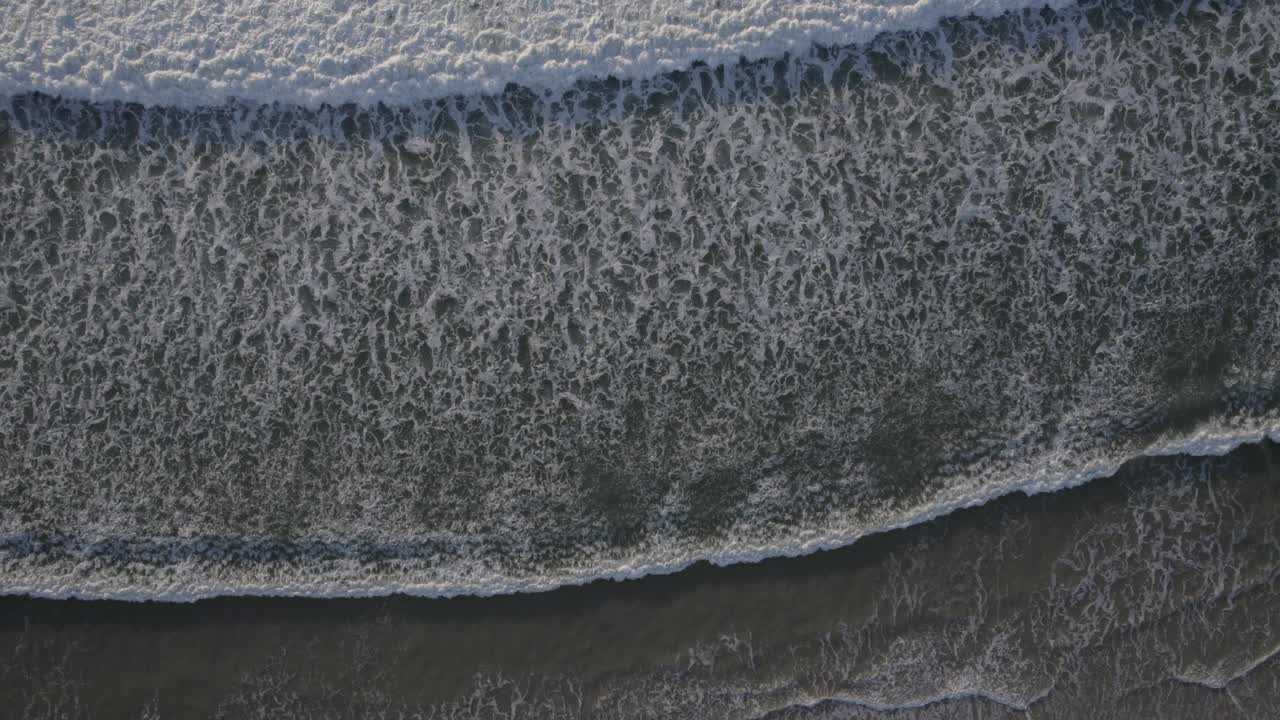 Top-down View Of White Foamy Waves Rolling At The Beach Shore