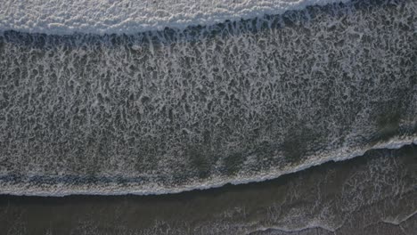 top-down view of white foamy waves rolling at the beach shore