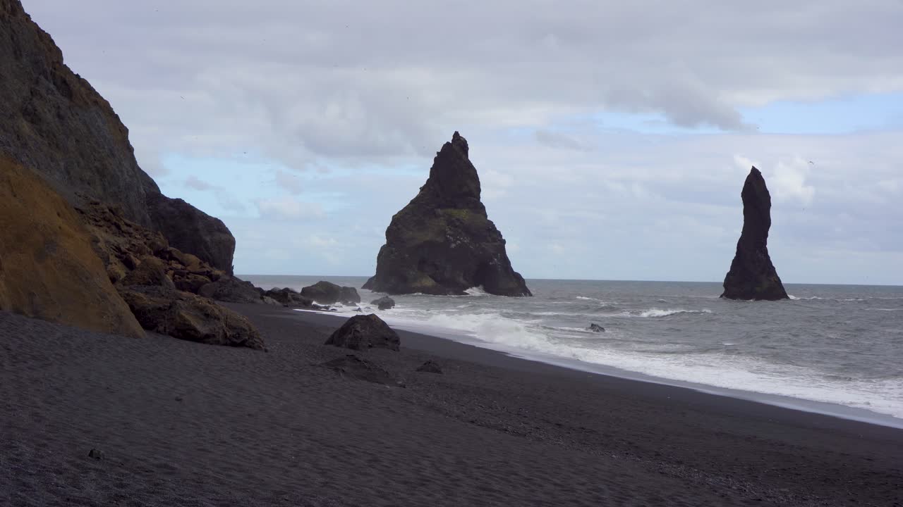 playa de arena negra con altas pilas de mar bajo un cielo nublado en islandia, paisaje costero dramático
