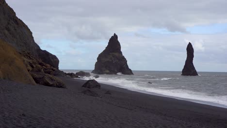 black sand beach with towering sea stacks under a cloudy sky in iceland, dramatic coastal landscape