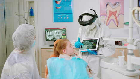 dentist in protective equipment showing on tablet dental x-ray reviewing it