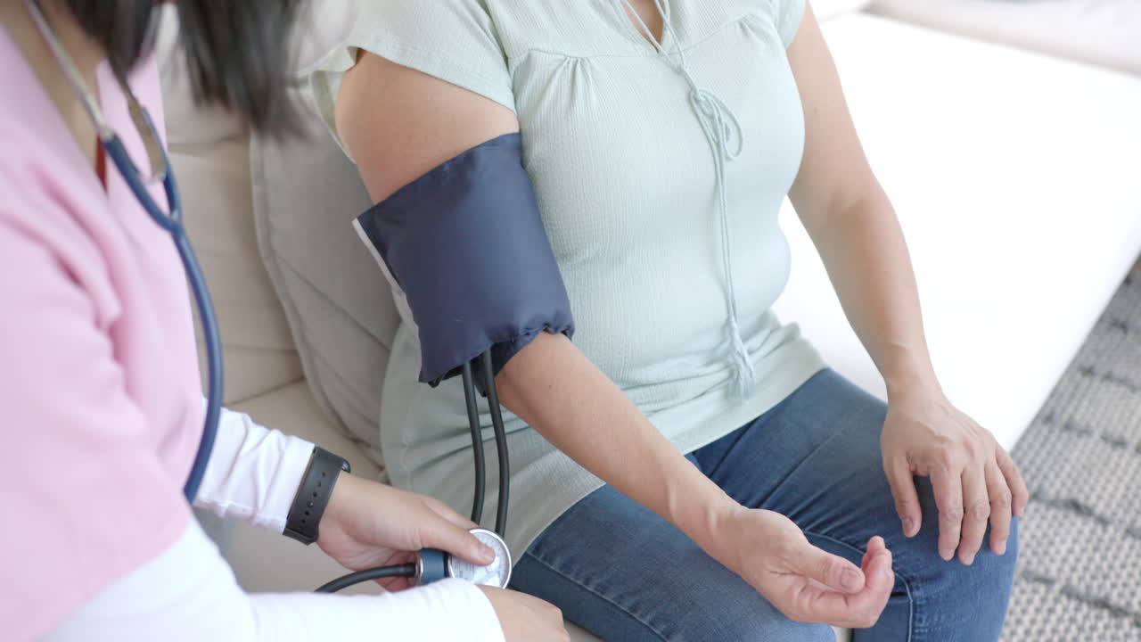 Taking blood pressure, healthcare professional assisting senior asian woman at home