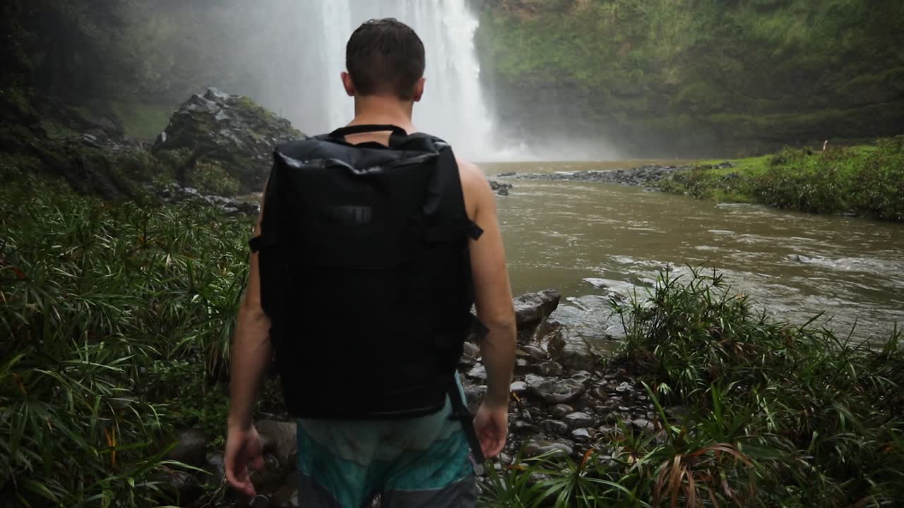joven excursionista masculino frente a la cascada de las cataratas wailua en kauai, hawaii