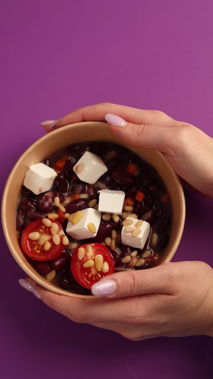 mujer sosteniendo un plato de ensalada de frijoles con feta y nueces de pino