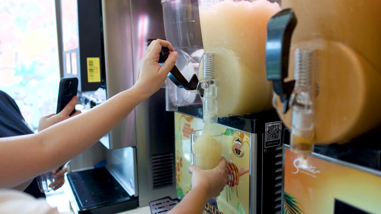 Seseorang mengisi gelas dengan minuman es serut beku dari dispenser komersial di sebuah restoran