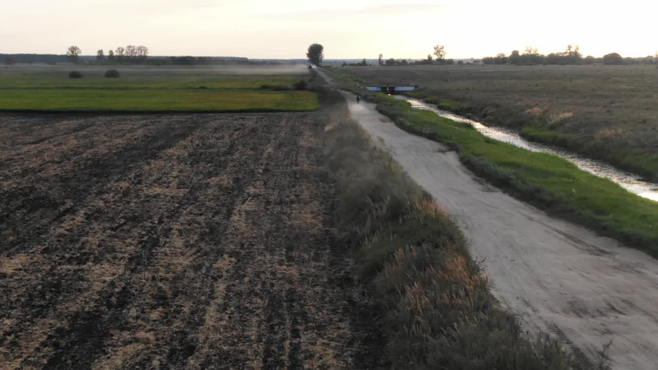 vista aérea de una motocicleta que baja por una carretera de tierra durante la puesta del sol