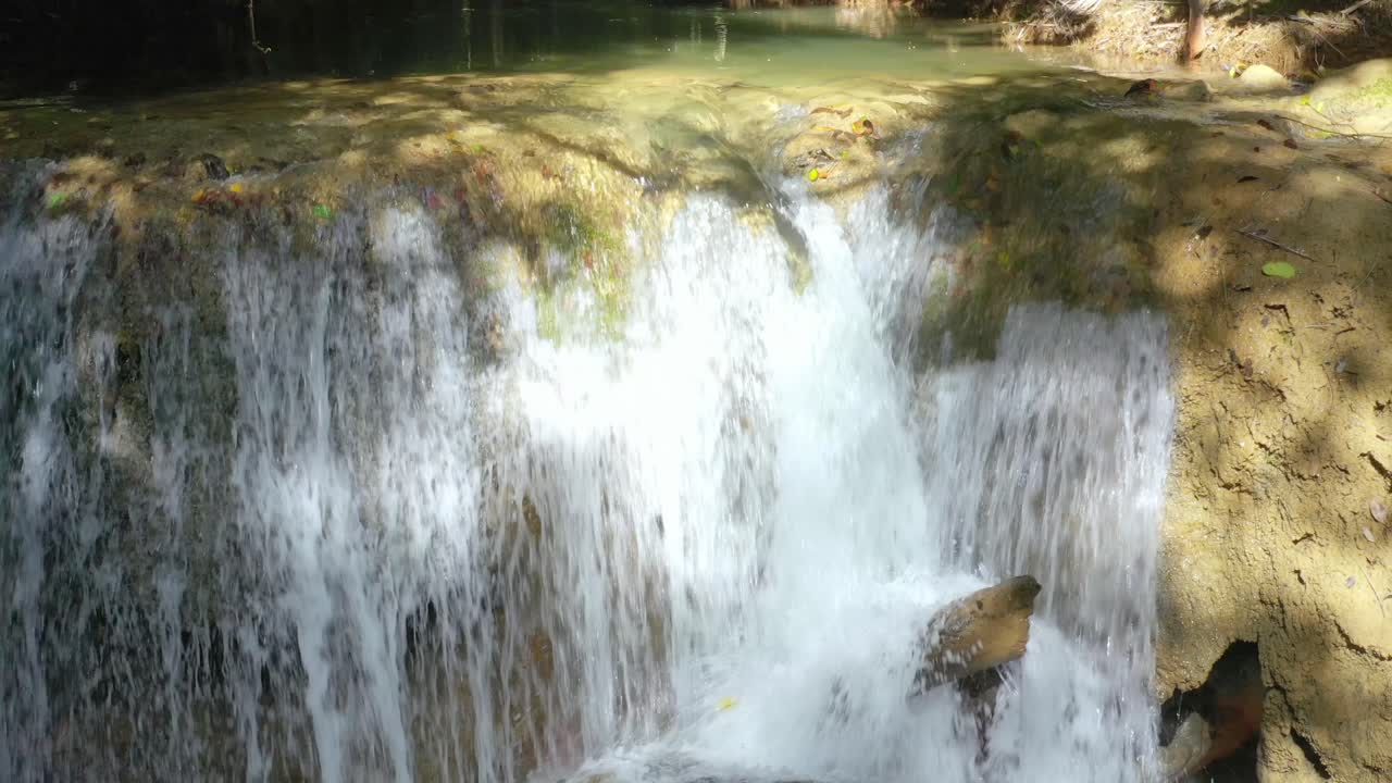 agua blanca clara y fresca cae en cascada por una pequeña pared de roca en el bosque natural junto a una gran piedra en el río, cierra la sartén hacia arriba