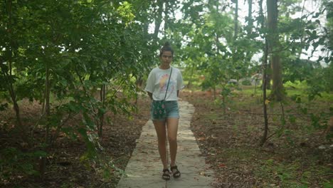 vista frontal de una mujer de piel marrón que camina paseando casualmente por un parque tropical