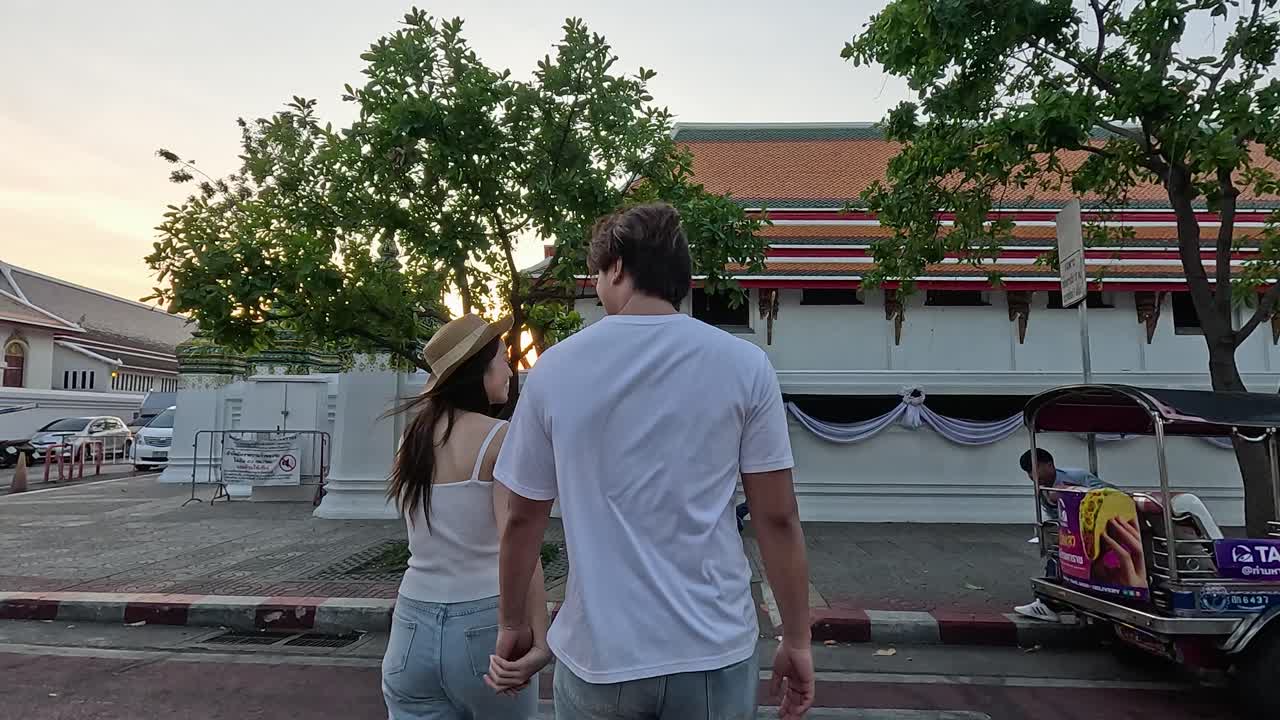 Rear view of tourist couple walking across crosswalk toward temple wall at golden hour