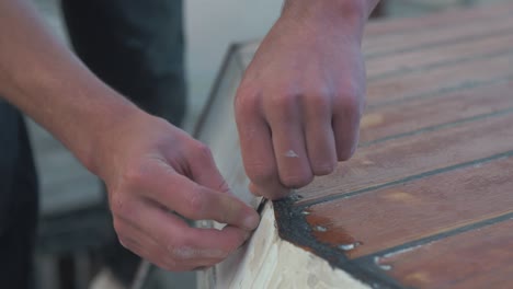 Limpieza-Raspando-El-Exceso-De-Sellador-Sikaflex-En-El-Techo-De-La-Cabina-De-Un-Barco-De-Madera