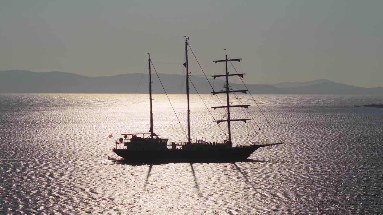 A majestic sailing ship with three masts reflects sunlight on the shimmering Aegean Sea surface