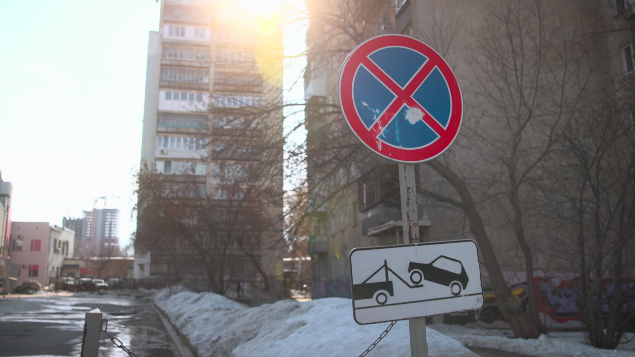 No Parking Sign By Snowy Urban Street, Sun Glare Over Apartment Tower, Tow Truck Pictogram On Board, Piled . Media