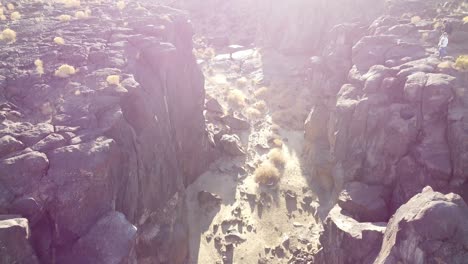 Tiro-Inclinado-Hacia-Abajo-Sobre-Terreno-Rocoso-Con-Grandes-Rocas-Y-Cantos-Rodados-A-Lo-Largo-Del-Cañón-Con-Lecho-De-Río-Seco-Con-Montañas-áridas-En-El-Fondo-En-Un-Día-Soleado