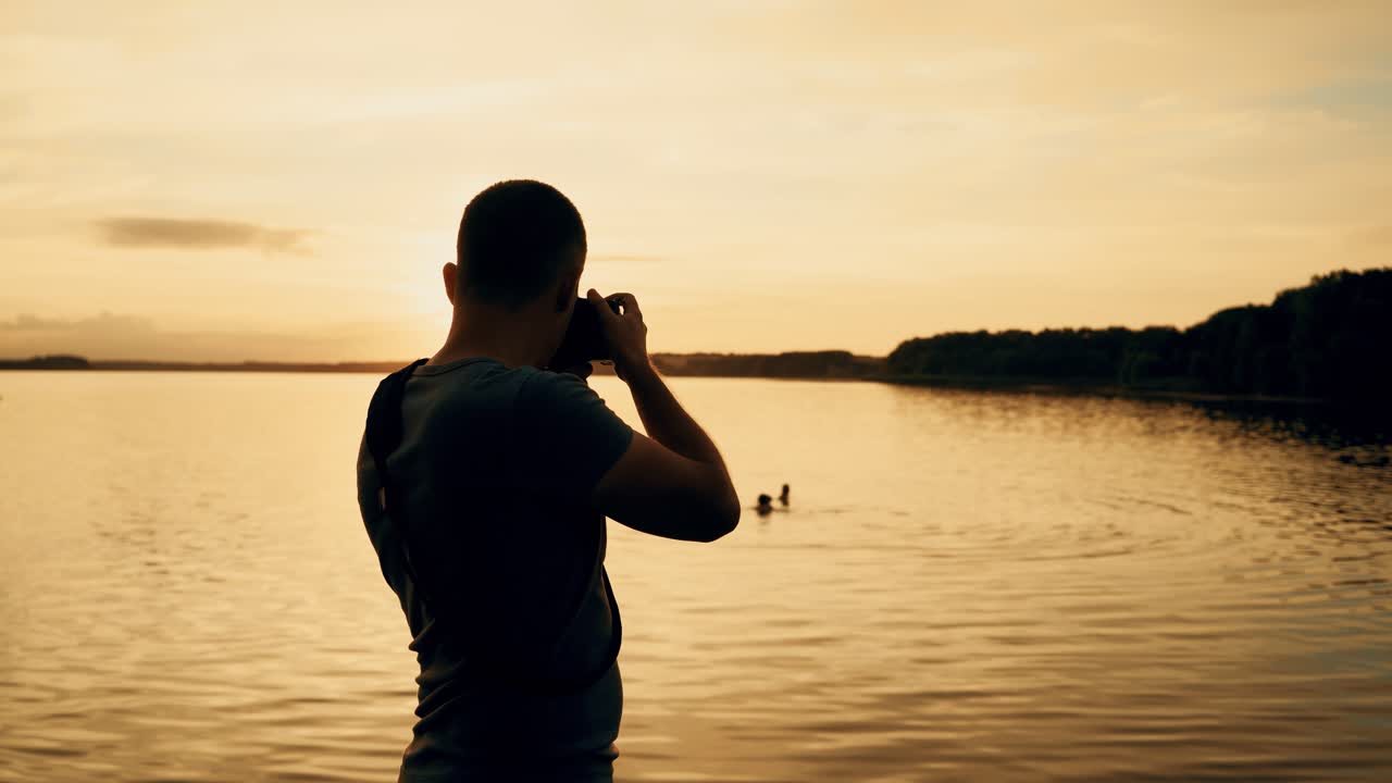 man with a camera in his hands makes a photo of the river on the background of sunset