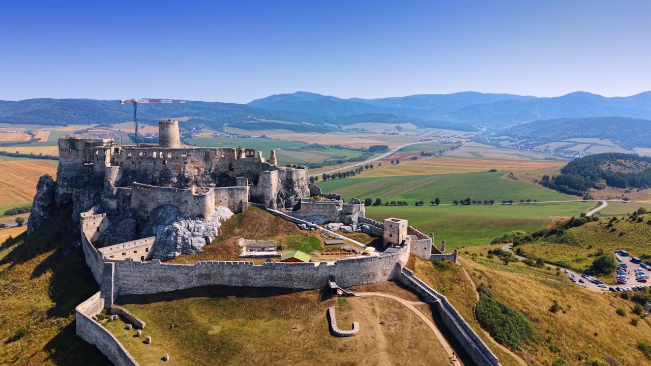 Un vecchio castello su una collina, circondato da campi verdi e montagne sullo sfondo, durante il giorno.