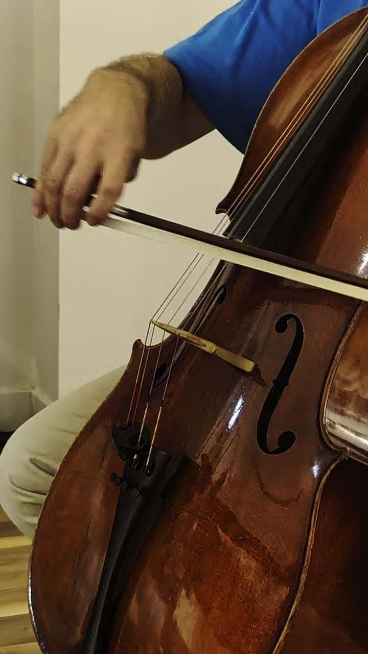 Close-up of a cellist’s hand bowing cello strings in casual attire