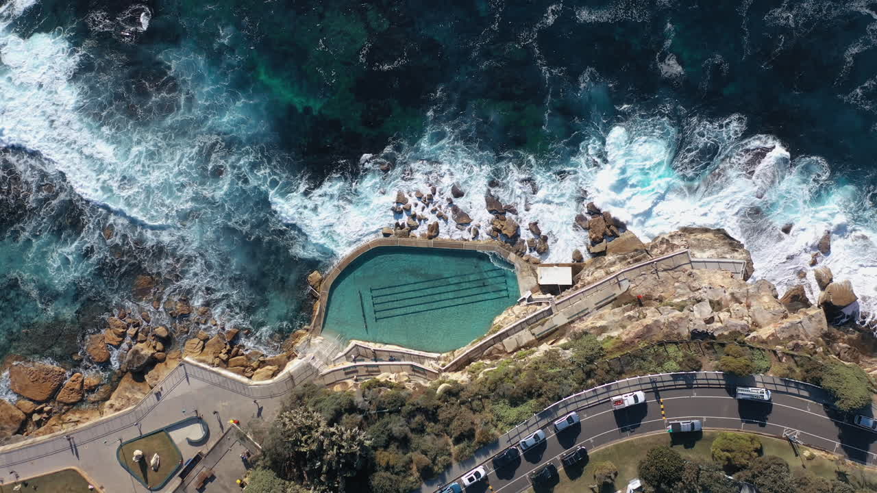 Rotating Aerial Top Down Of Coastal Rock Pool And Busy Coastline Road In Sydney