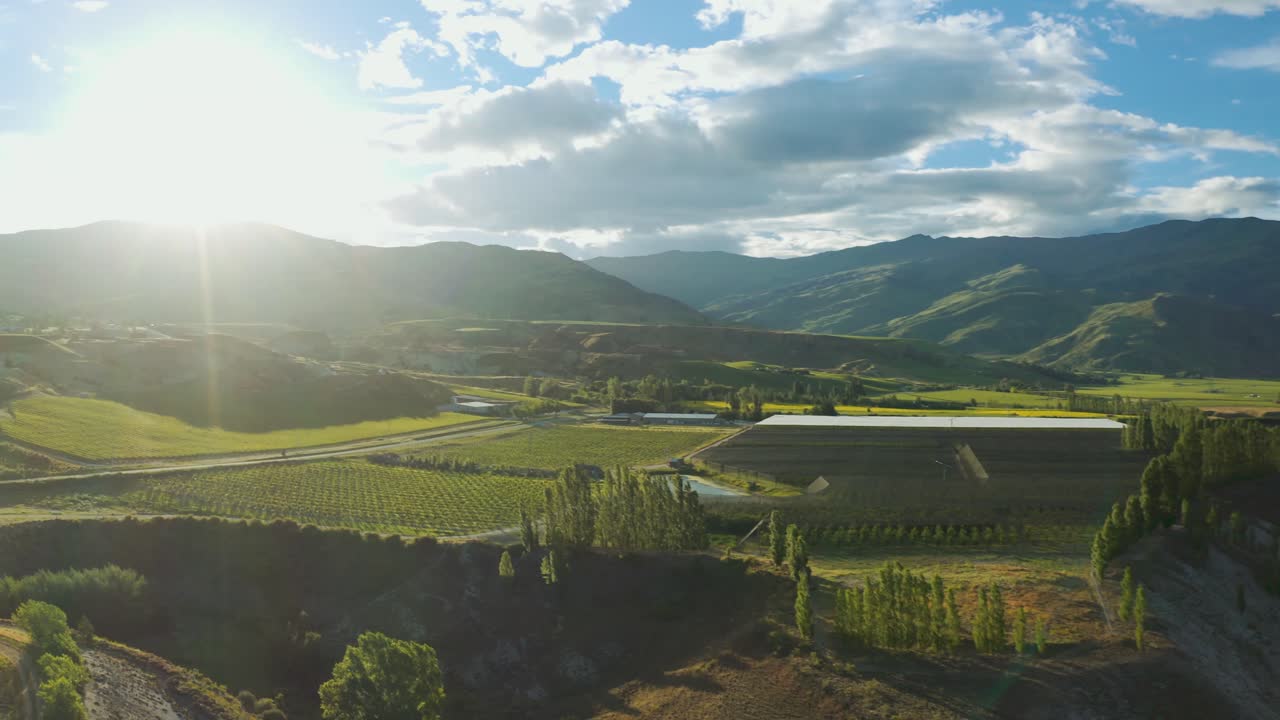 Tracciamento aereo all'indietro sopra i vigneti nel Central Otago, sopra un fiume, con un bagliore solare sull'obiettivo
