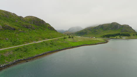 Cinematic-overview-shot-of-a-camper-van-driving-on-a-scenic-route-through-the-landscape-of-the-Lofoten-Islands-in-Norway,-Europe