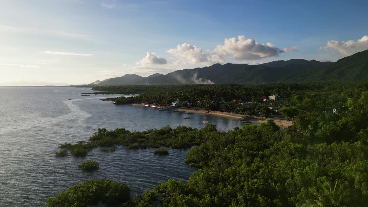 Scenic aerial view of a quaint barangay town amid lush greenery, peaceful coastline, and mountain backdrop at tropical island Catanduanes, Philippines.