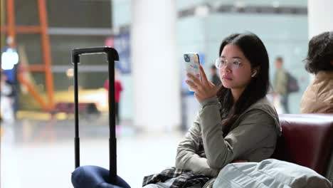 a woman sits and waits for her flight to be called while using her smartphone at the boarding gate in beijing international airport, china.